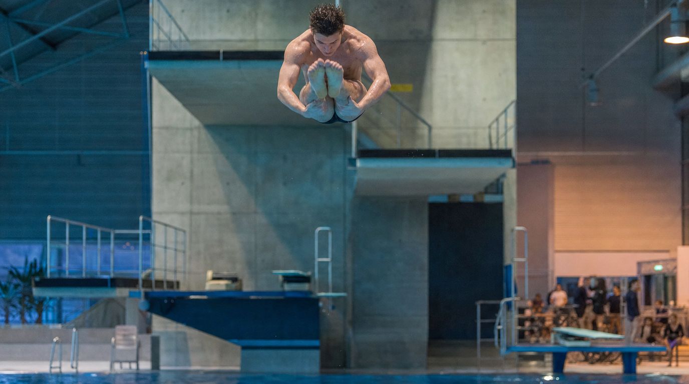 Turmspringer in gestreckter Haltung kurz vor dem Eintauchen in ein Sprungbecken einer Schwimmhalle